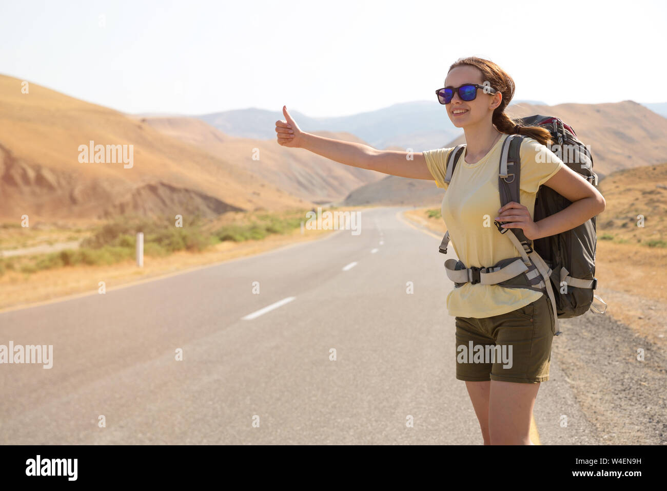 Auto-stoppeur femme voyageur sur la route dans le coucher du soleil. Girl traveler randonneur sur la route. Vacances d'été. La liberté. Banque D'Images