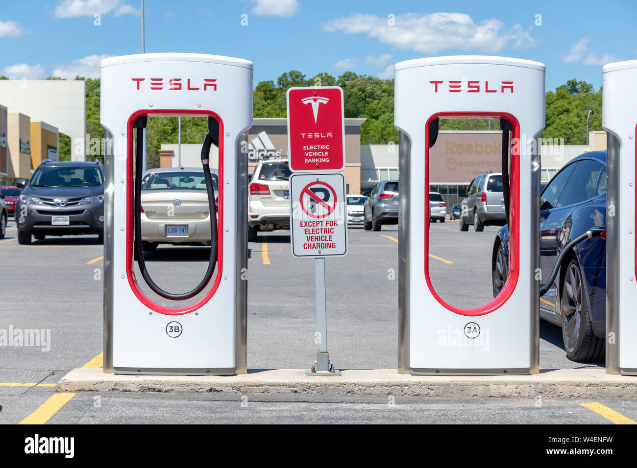 Tesla Supercharger cale à Kingston, en Ontario, avec parking gratuit et des signes d'obstruction Tesla Model S bleu chargement dans l'arrière-plan. Banque D'Images Tesla Supercharger cale à Kingston, en Ontario, avec parking gratuit et des signes d'obstruction Tesla Model S bleu chargement dans l'arrière-plan. Banque D'Images