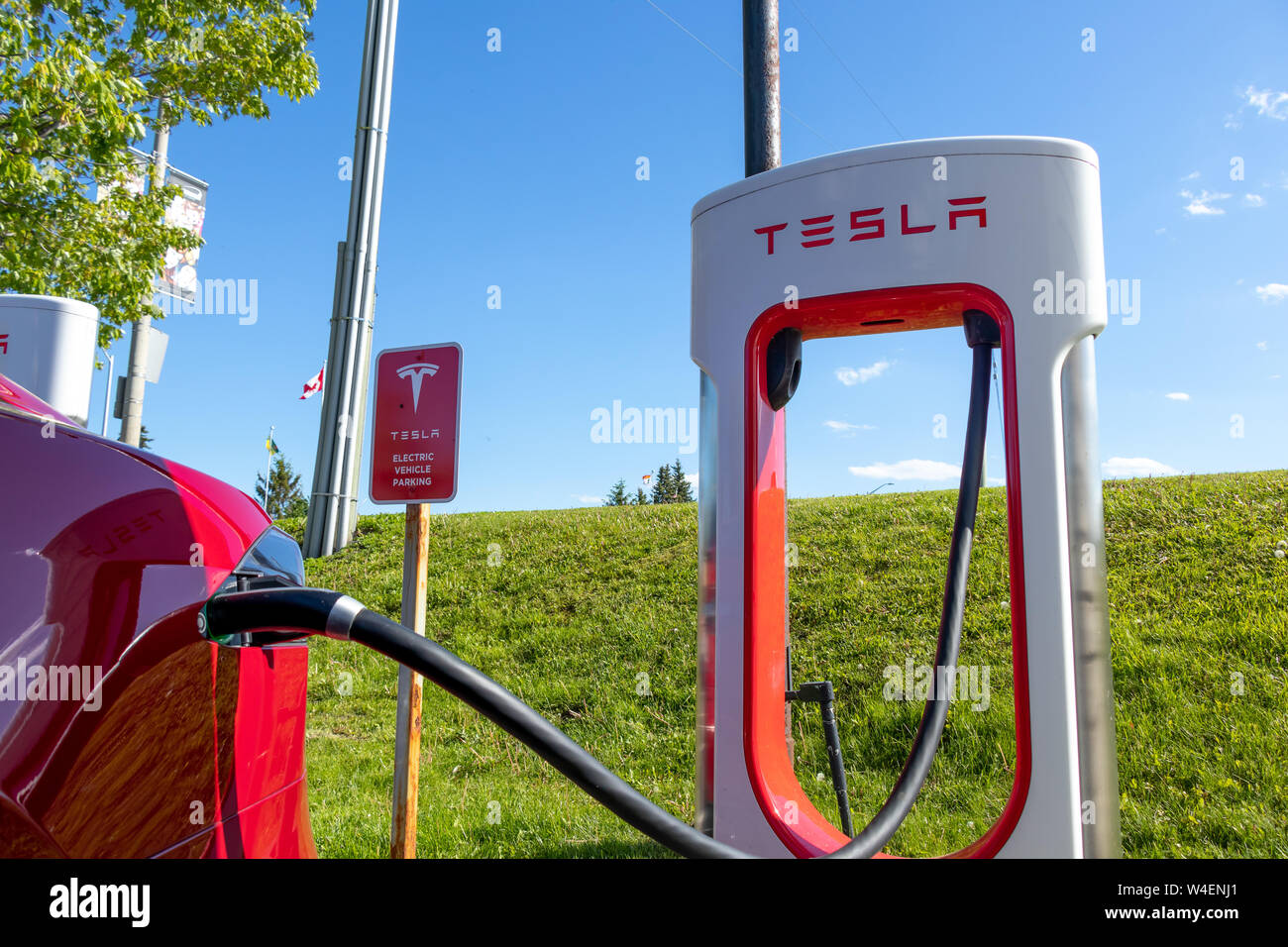 La station a de Tesla Tesla et signe avec véhicule Véhicule électrique branché en charge, sur une journée ensoleillée. Banque D'Images La station a de Tesla Tesla et signe avec véhicule Véhicule électrique branché en charge, sur une journée ensoleillée. Banque D'Images