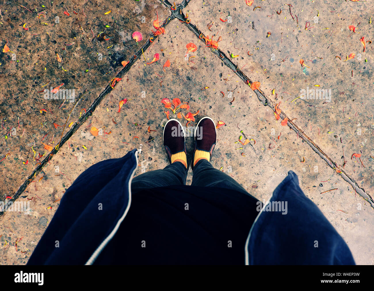 Vue de dessus de pieds femme en noir étendoir cour extérieure avec chute de pétales orange matin pluvieux Banque D'Images