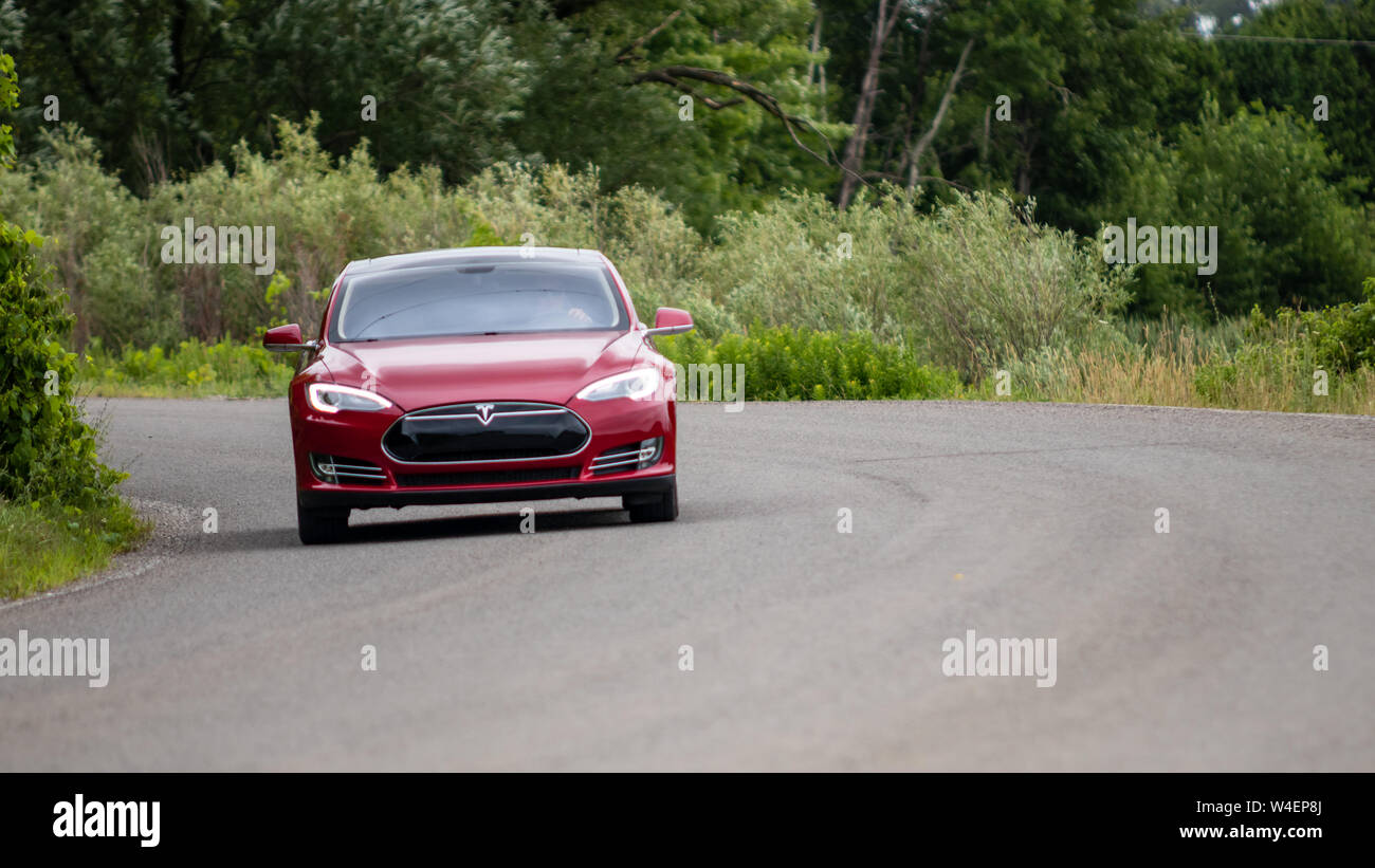 Model S aller autour d'un coin sur la route d'arbres remplis pendant une journée nuageuse. Banque D'Images