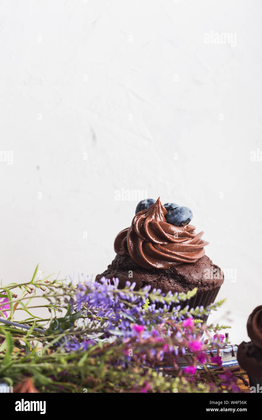 Des petits gâteaux au chocolat avec crème au beurre et les bleuets sur tableau blanc, bouquet de fleurs sauvages, Close up, délicieux dessert de fête Banque D'Images