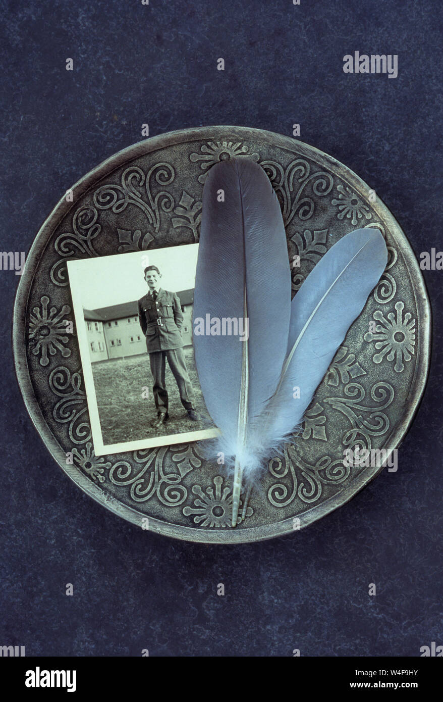 Plat en argent ouvragée contenant photo en noir et blanc de 1940, jeune homme en uniforme militaire et deux plumes de pigeon gris Banque D'Images Plat en argent ouvragée contenant photo en noir et blanc de 1940, jeune homme en uniforme militaire et deux plumes de pigeon gris Banque D'Images