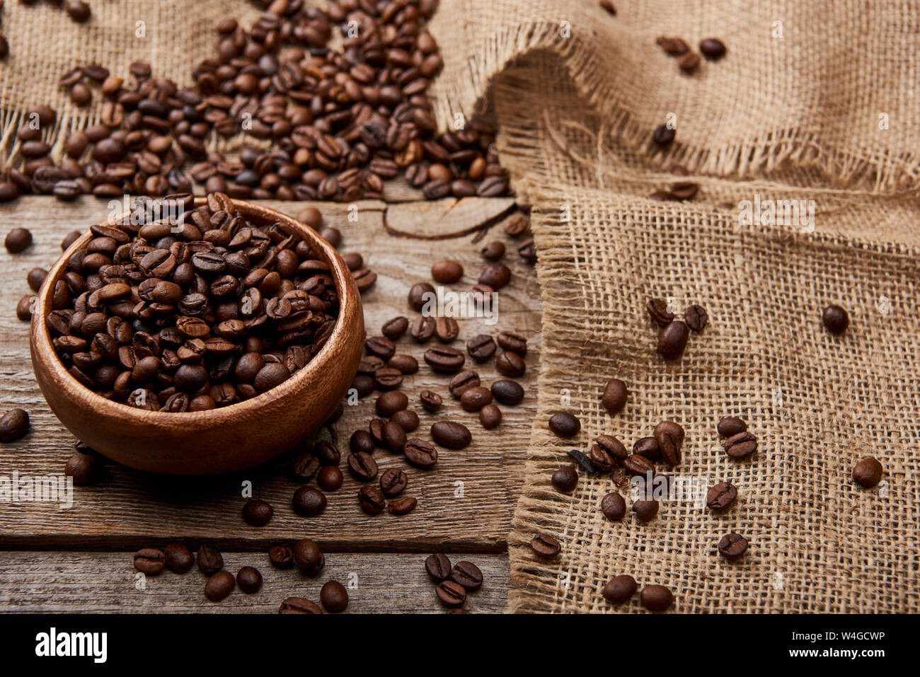 Les grains de café torréfié frais dans un bol en bois sur le bord d'un sac Banque D'Images