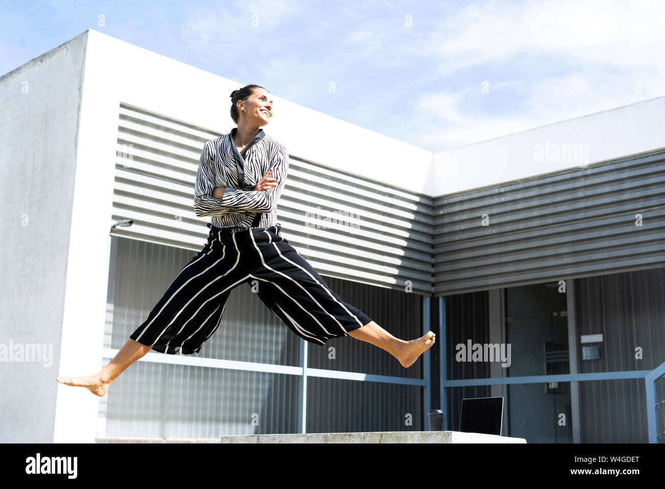 Ballerine femme sautant sur un banc en face d'un immeuble de bureaux Banque D'Images