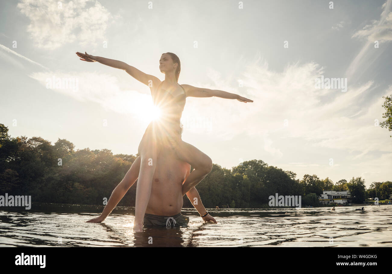 Jeune femme assise sur les épaules du jeune homme debout dans le lac, profiter du soleil Banque D'Images