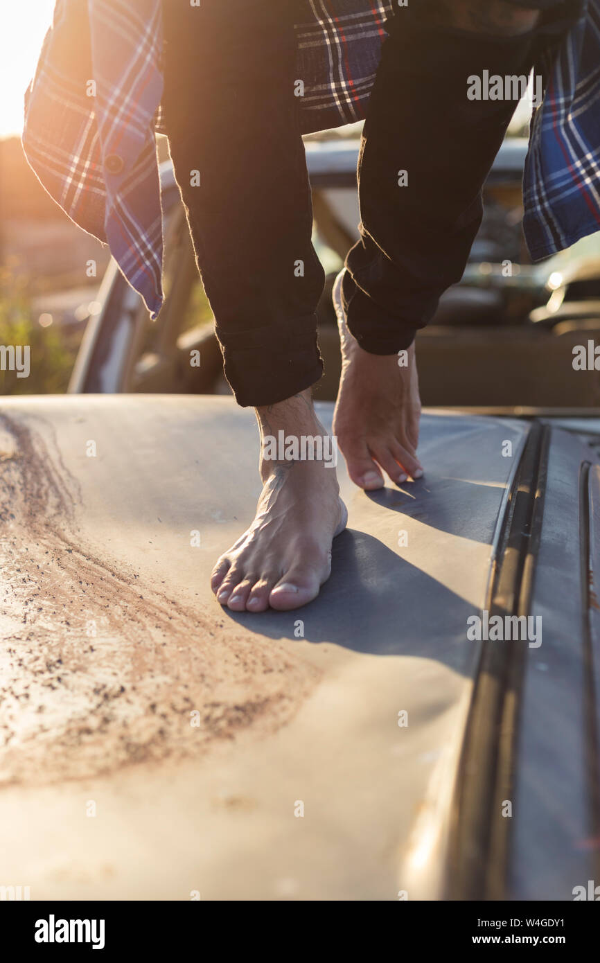 Jeune homme marchant pieds nus sur le toit du véhicule sur un parc à ferrailles Banque D'Images