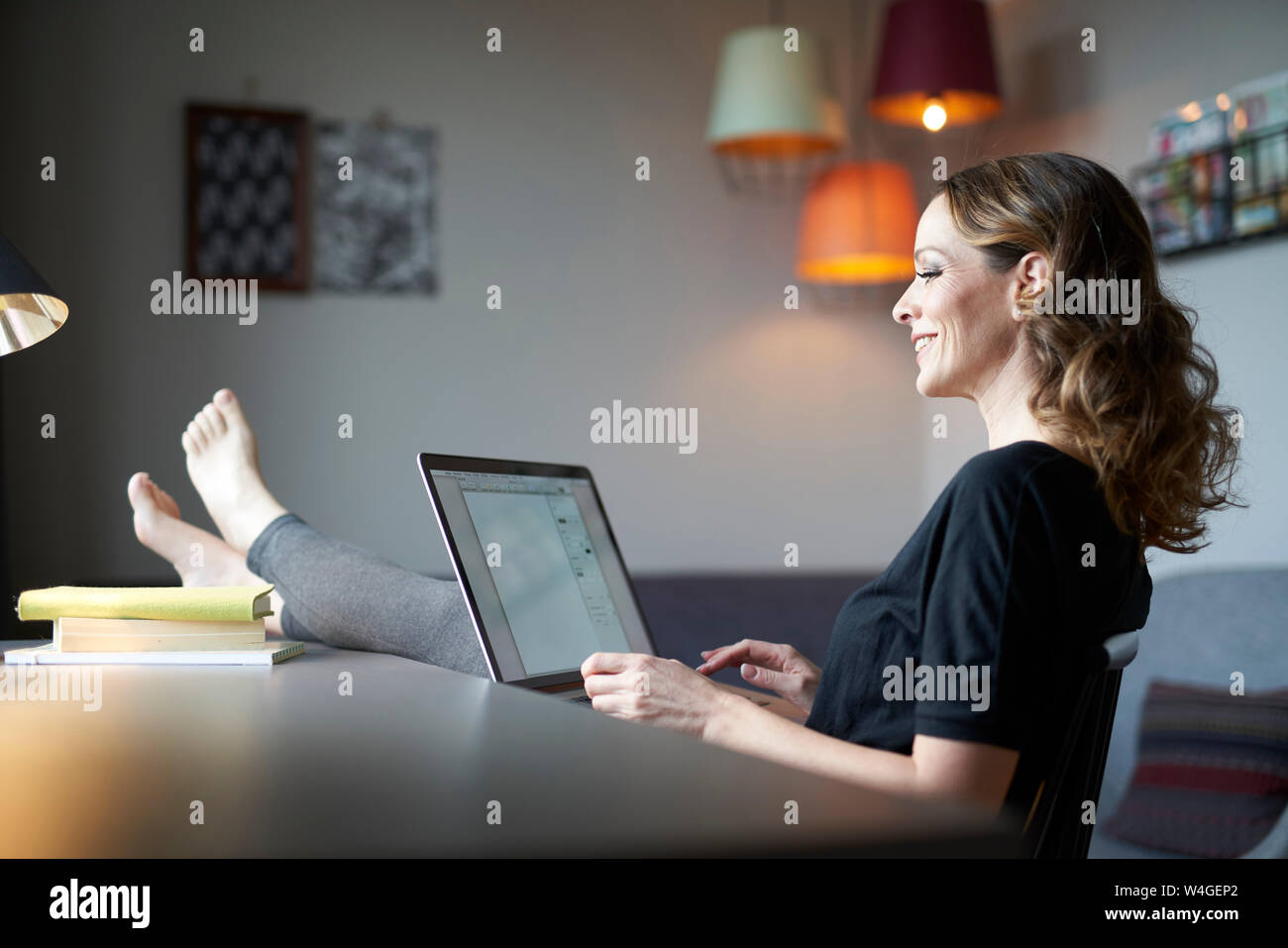 Smiling woman using laptop at home avec les pieds sur la table Banque D'Images