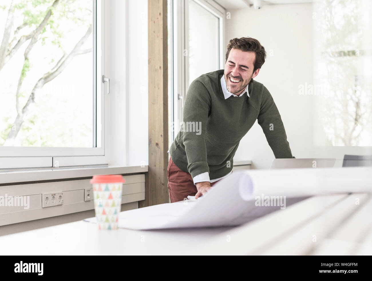 Rire jeune architecte travaillant sur blueprint in bright office Banque D'Images