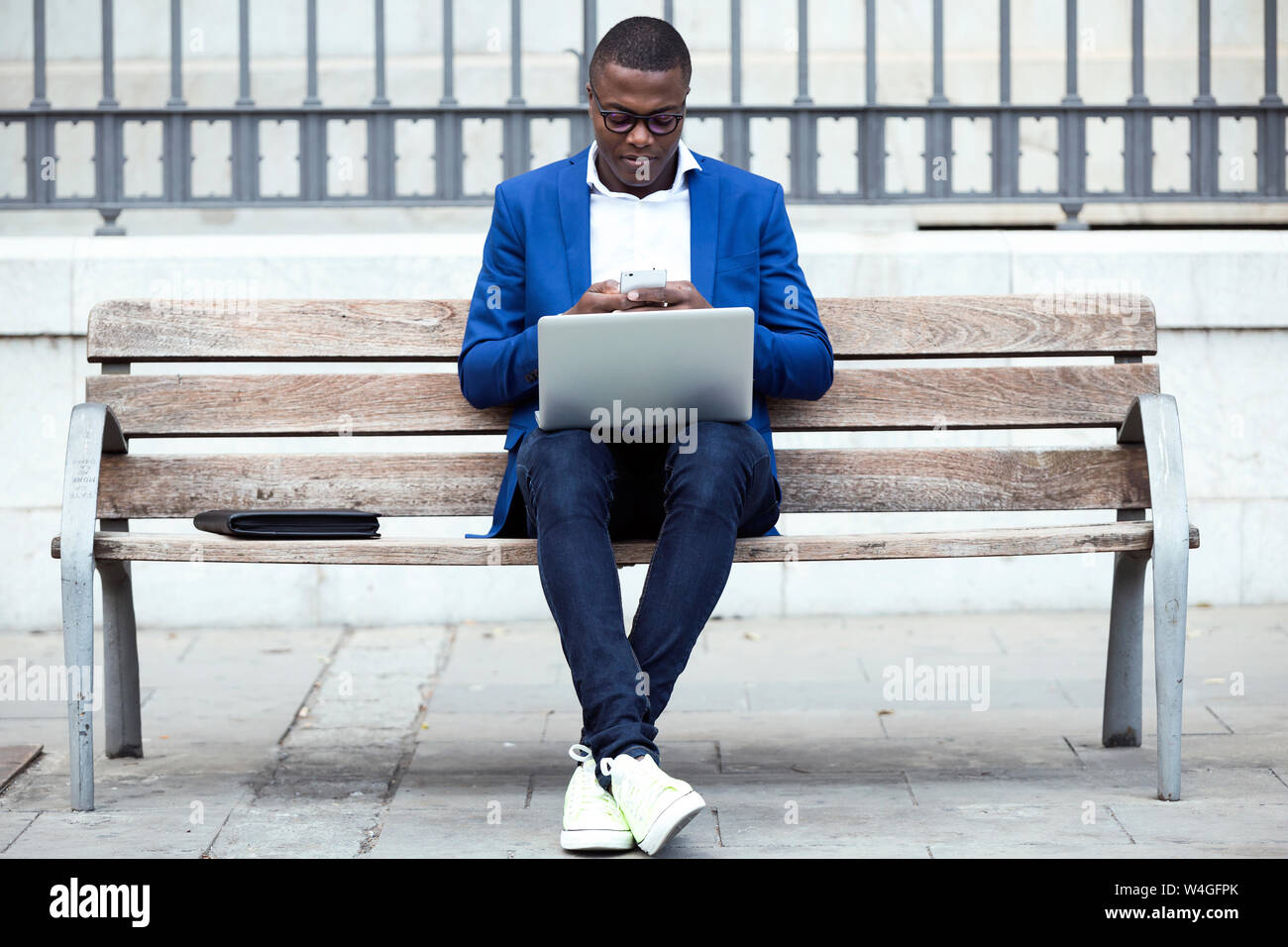 Young businessman wearing blue veste de costume sitting on bench and using laptop Banque D'Images