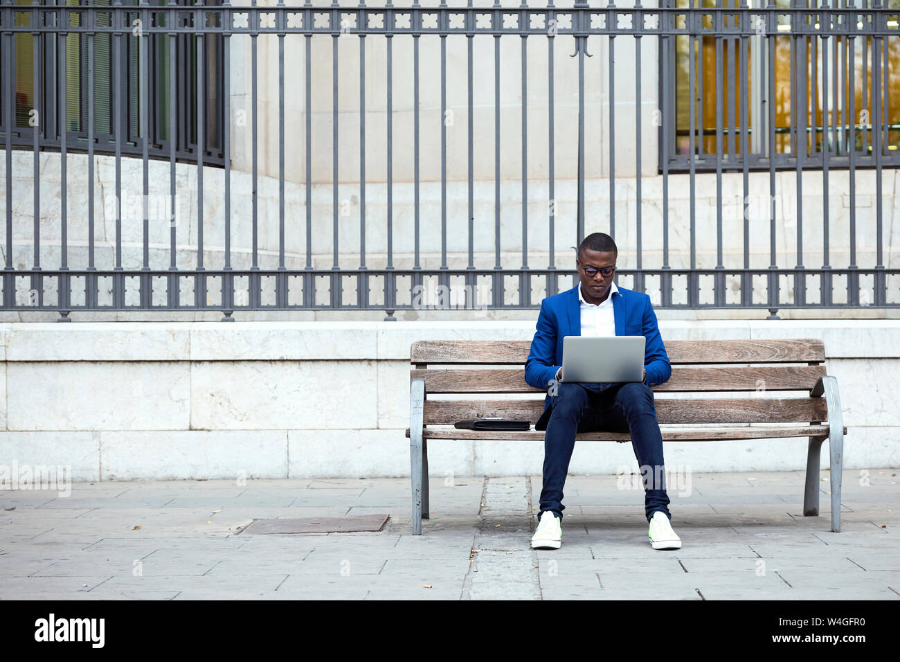 Young businessman wearing blue veste de costume sitting on bench and using laptop Banque D'Images