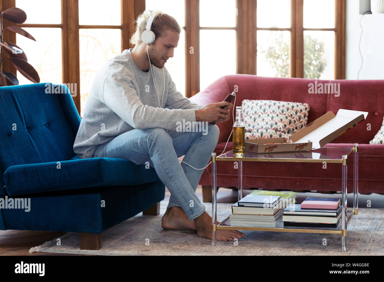 Young man sitting on couch with cell phone et écouteurs Banque D'Images