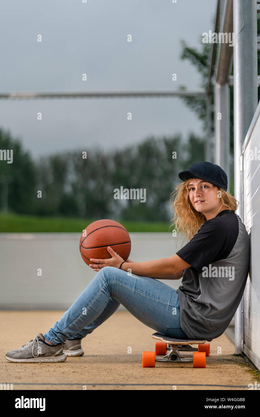 Jeune femme avec le basket-ball assis sur planche Banque D'Images