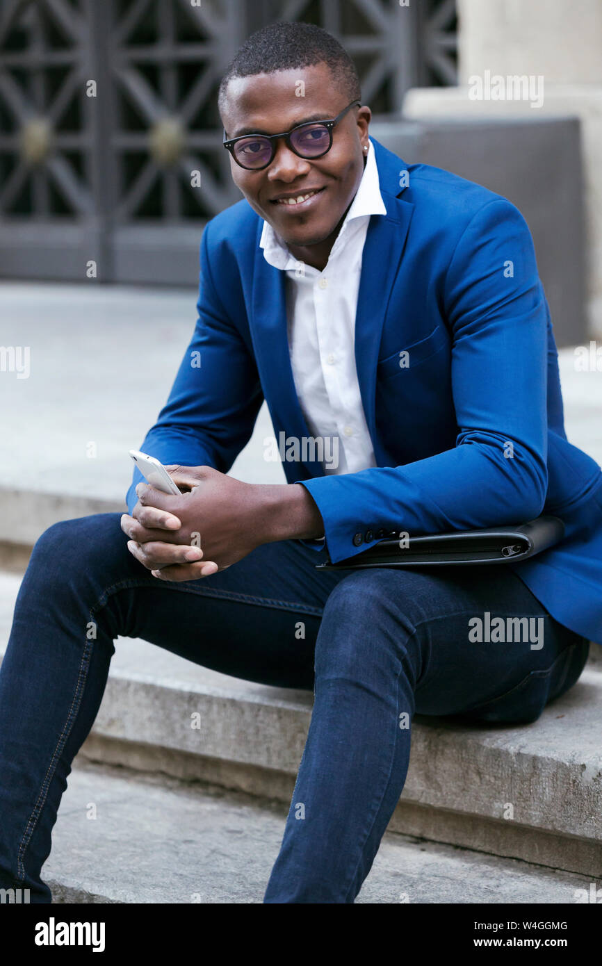Young businessman wearing blue veste de costume, assis sur l'étape et holding smartphone Banque D'Images