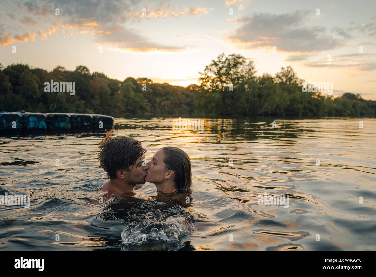 Jeune couple kissing, nager dans le lac au coucher du soleil Banque D'Images