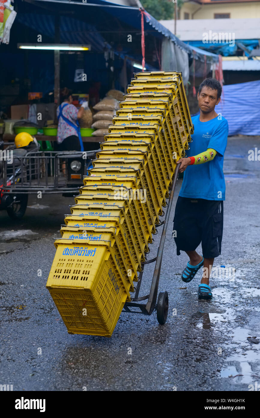 Un travailleur migrant du Myanmar (Birmanie) dans un marché en Thaïlande, le transport de caisses en plastique empilées ; Lieu : La ville de Phuket, Thaïlande Banque D'Images