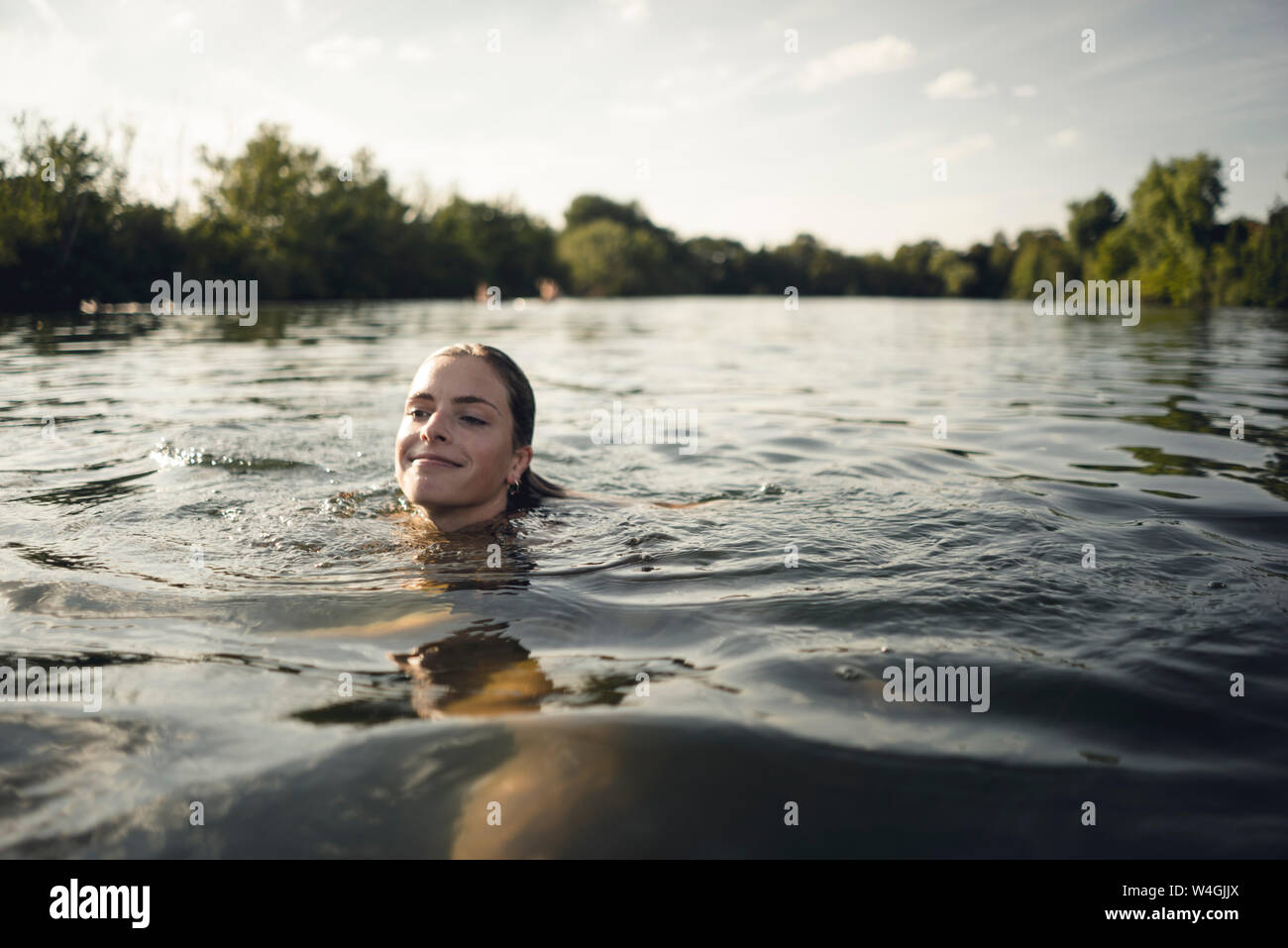 Jeune femme natation dans le lac en été, smiling Banque D'Images