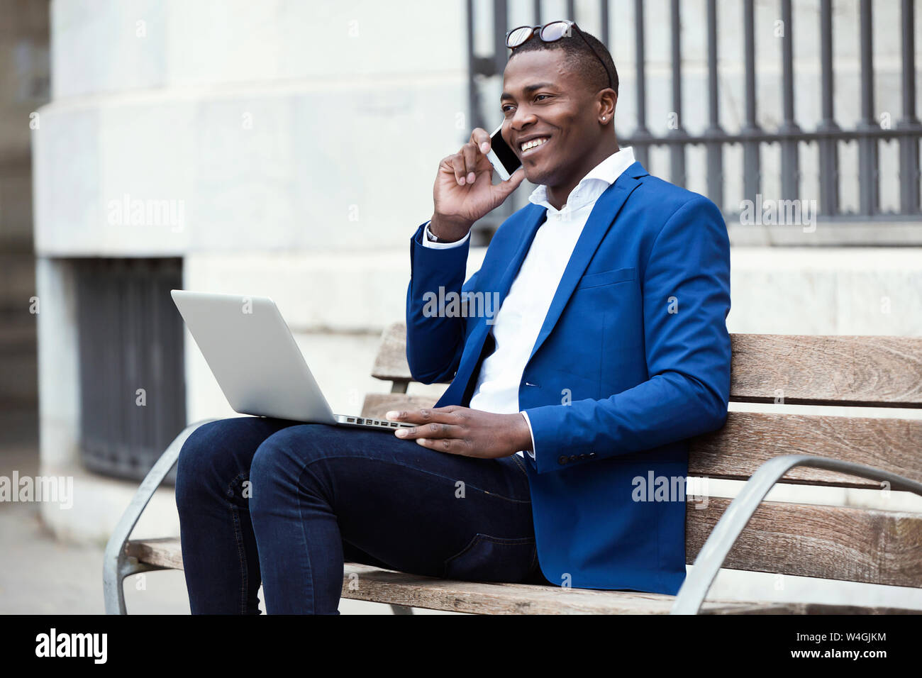 Young businessman wearing blue veste de costume assis sur un banc et using smartphone Banque D'Images