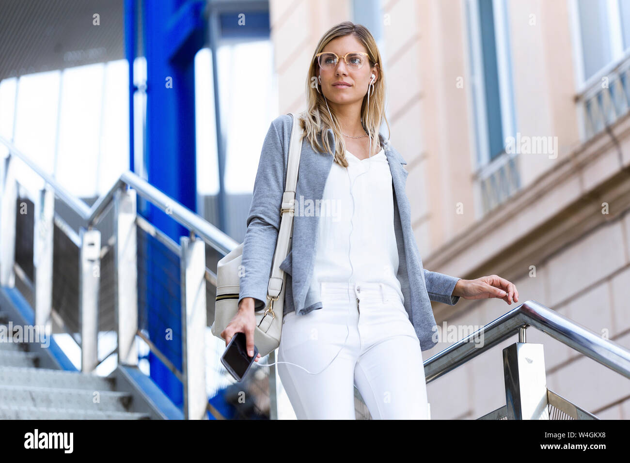 Young businesswoman à écouter de la musique avec un téléphone mobile tout en descendant des escaliers Banque D'Images