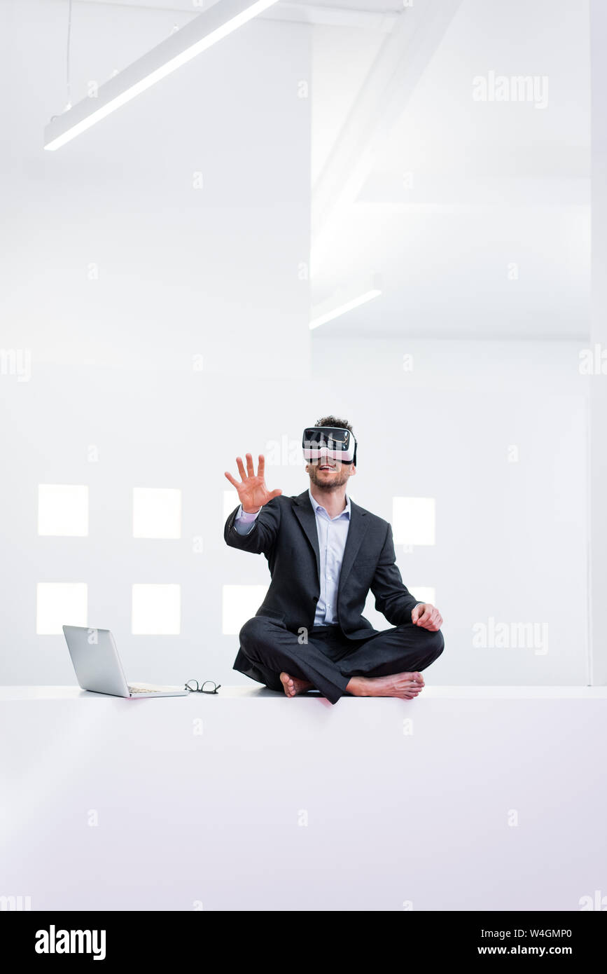 Businessman wearing glasses VR next to laptop in office Banque D'Images