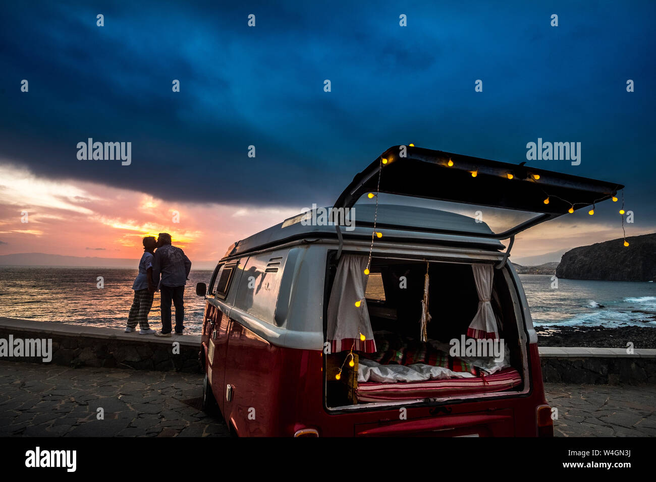 Senior couple voyageant dans un van, les baisers au coucher du soleil au bord de la mer Banque D'Images