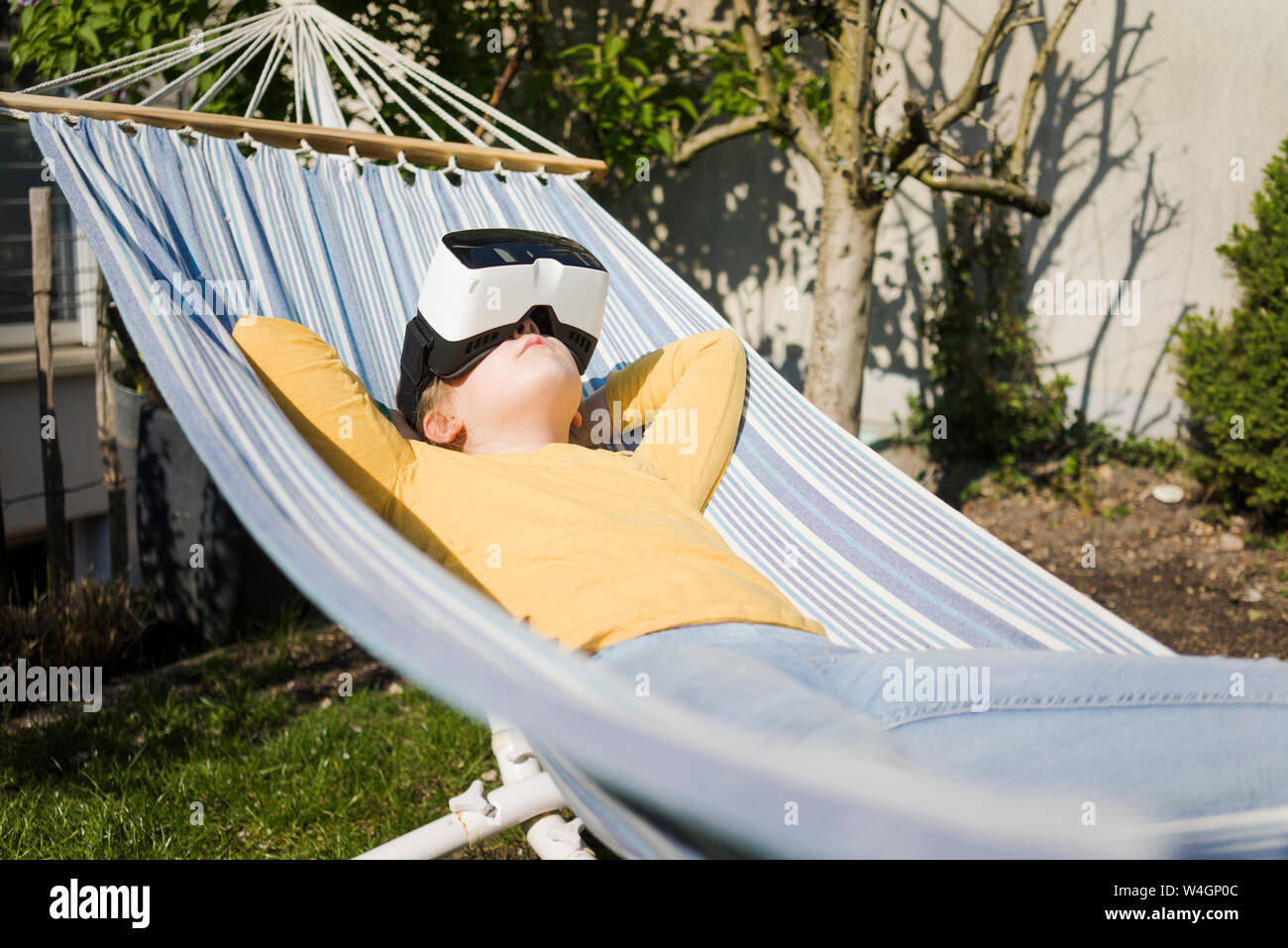 Girl lying in hammock en portant des lunettes VR jardin Banque D'Images