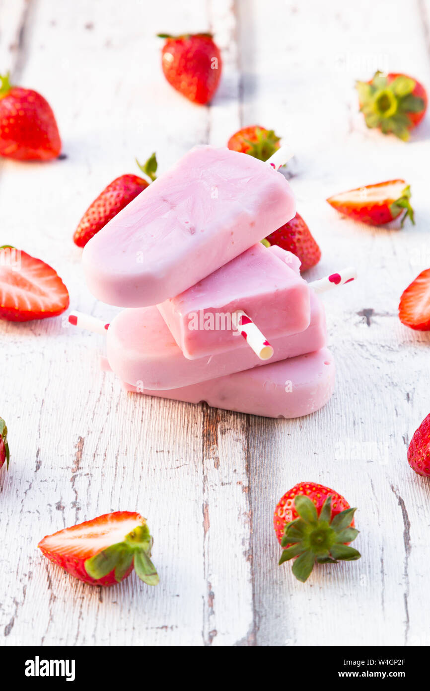 Yogourt aux fraises maison empilés sucettes glacées avec fraises fraîches sur bois blanc Banque D'Images