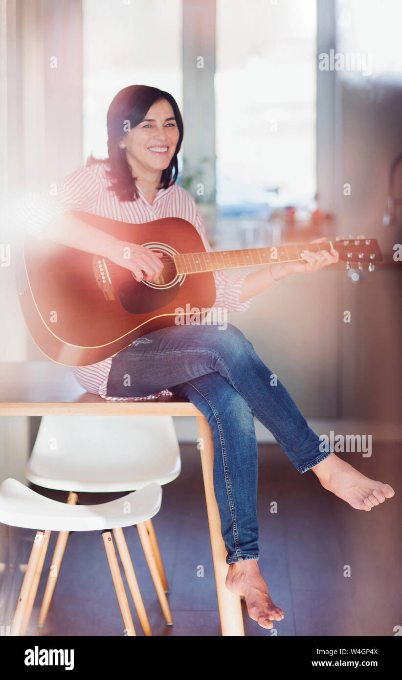 Smiling mature woman playing guitar at home Banque D'Images