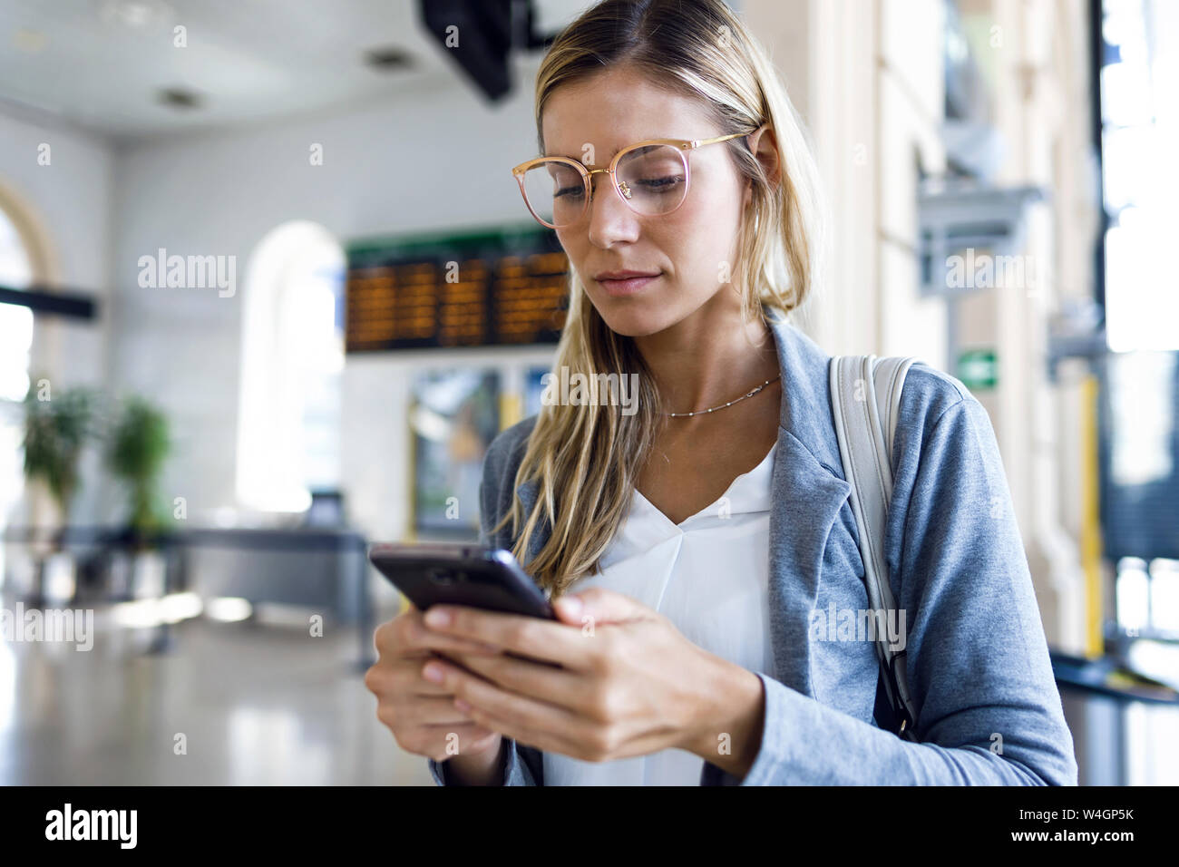 Jeune femme textos avec son téléphone portable dans le hall de la gare Banque D'Images