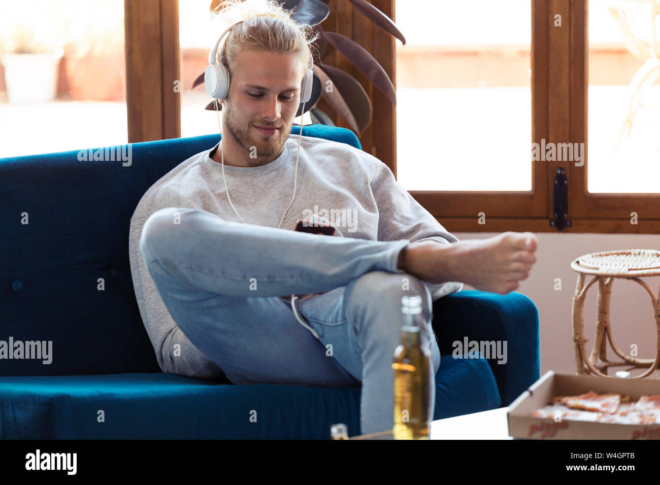 Young man sitting on couch with cell phone et écouteurs Banque D'Images