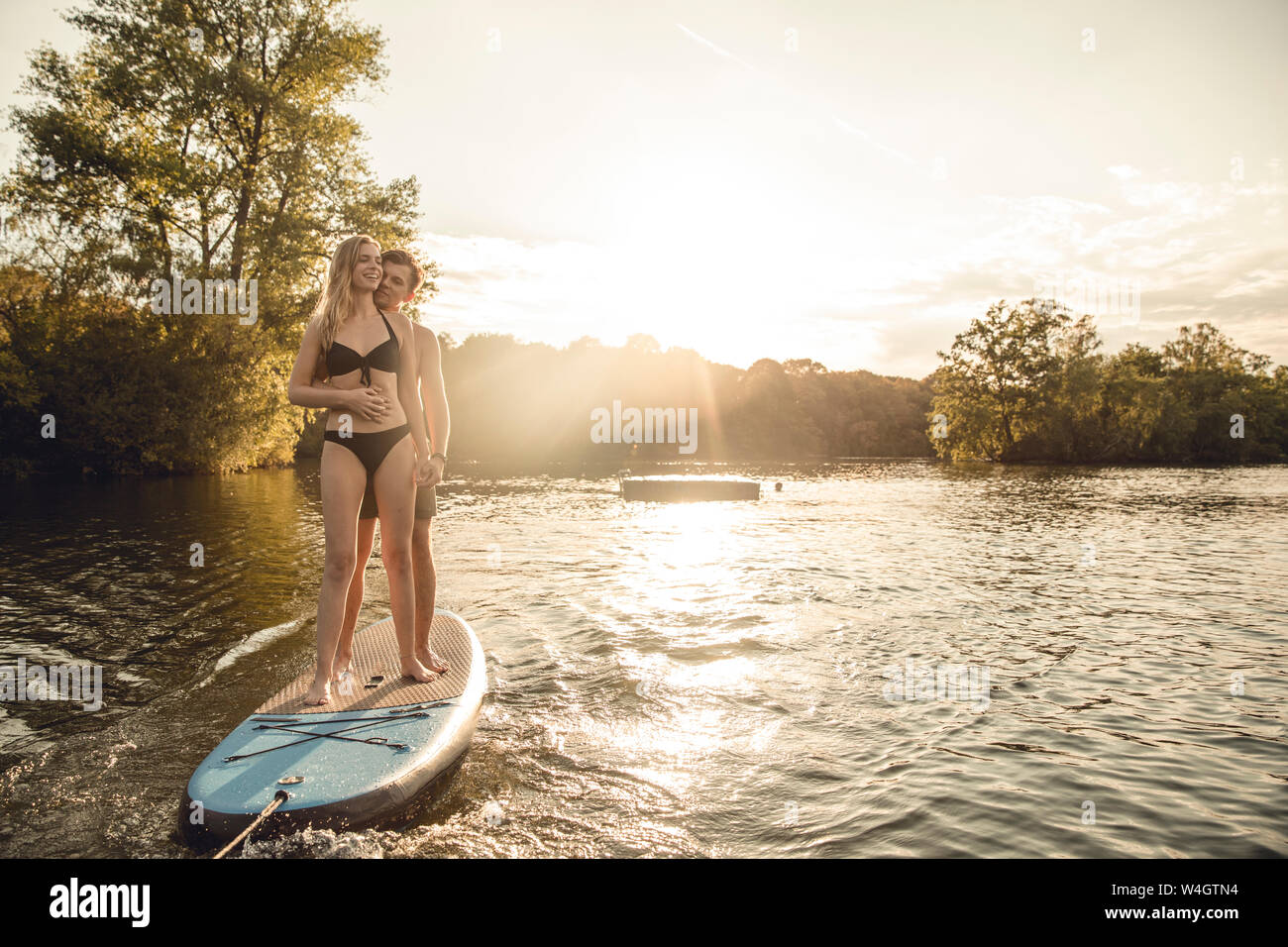 Jeune couple bénéficiant d'été au bord du lac, debout sur un paddleboard Banque D'Images