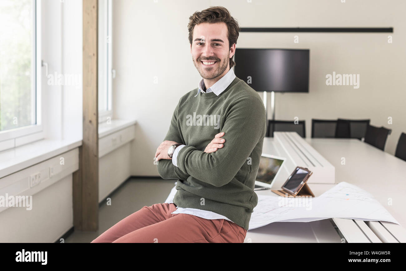 Succès, young businessman sitting in boardroom with arms crossed Banque D'Images