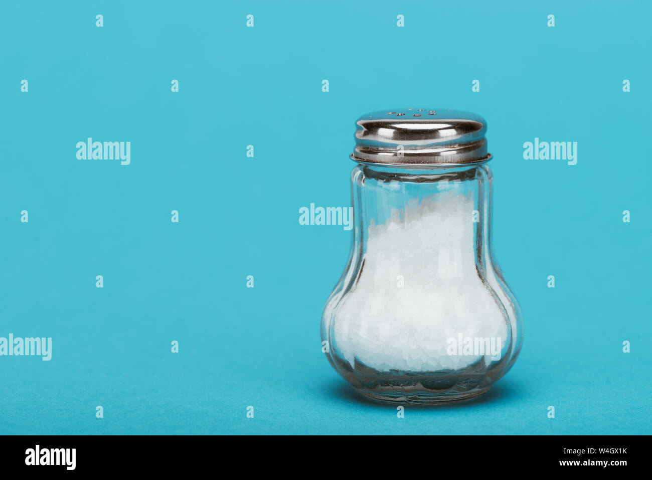 Des cristaux de sel dans la salière en verre avec bouchon métallique sur fond bleu avec copie espace Banque D'Images