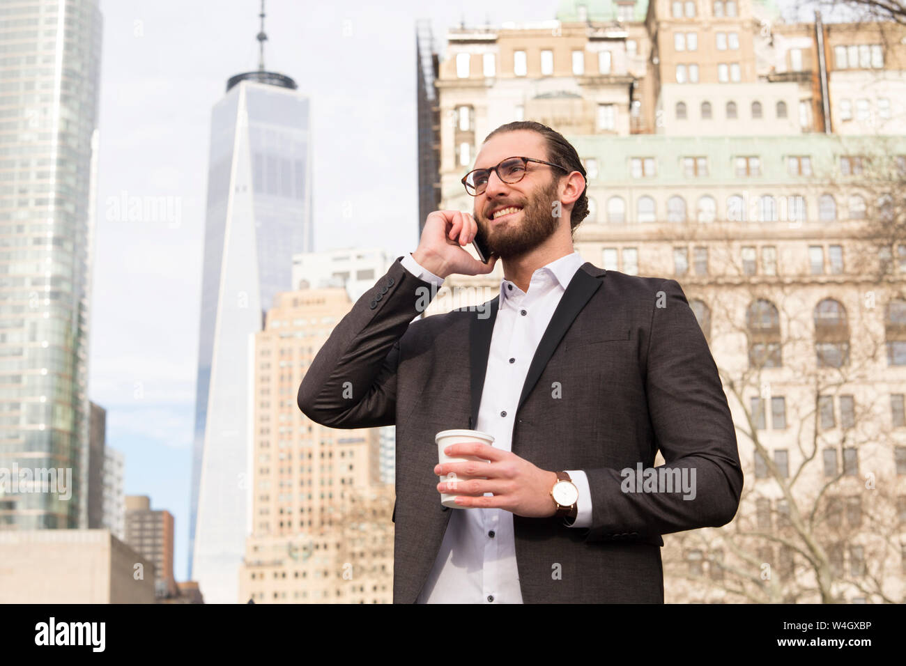 Smiling young businessman with coffee pour aller au téléphone, New York City, USA Banque D'Images