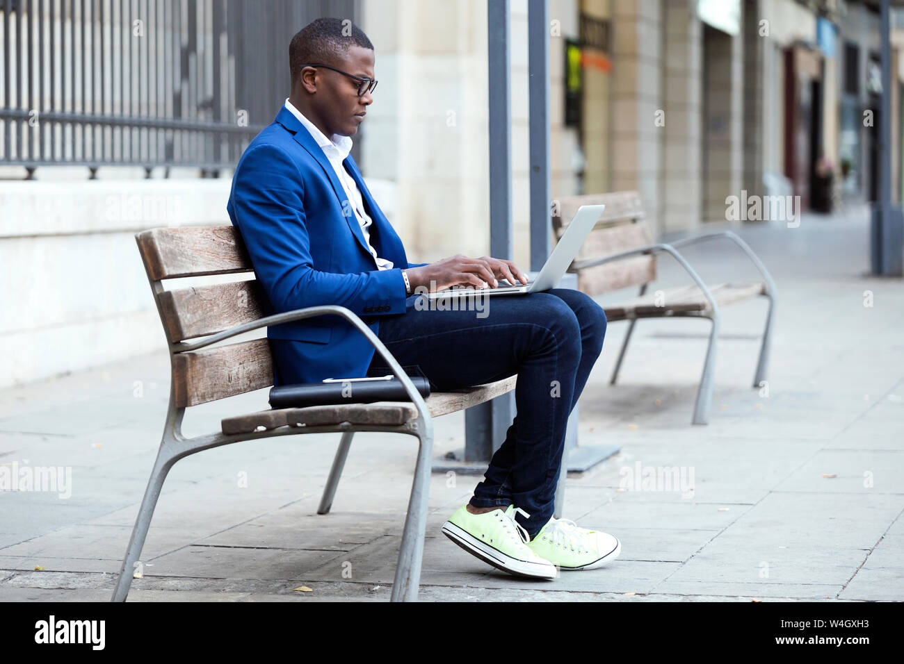 Young businessman wearing blue veste de costume sitting on bench and using laptop Banque D'Images