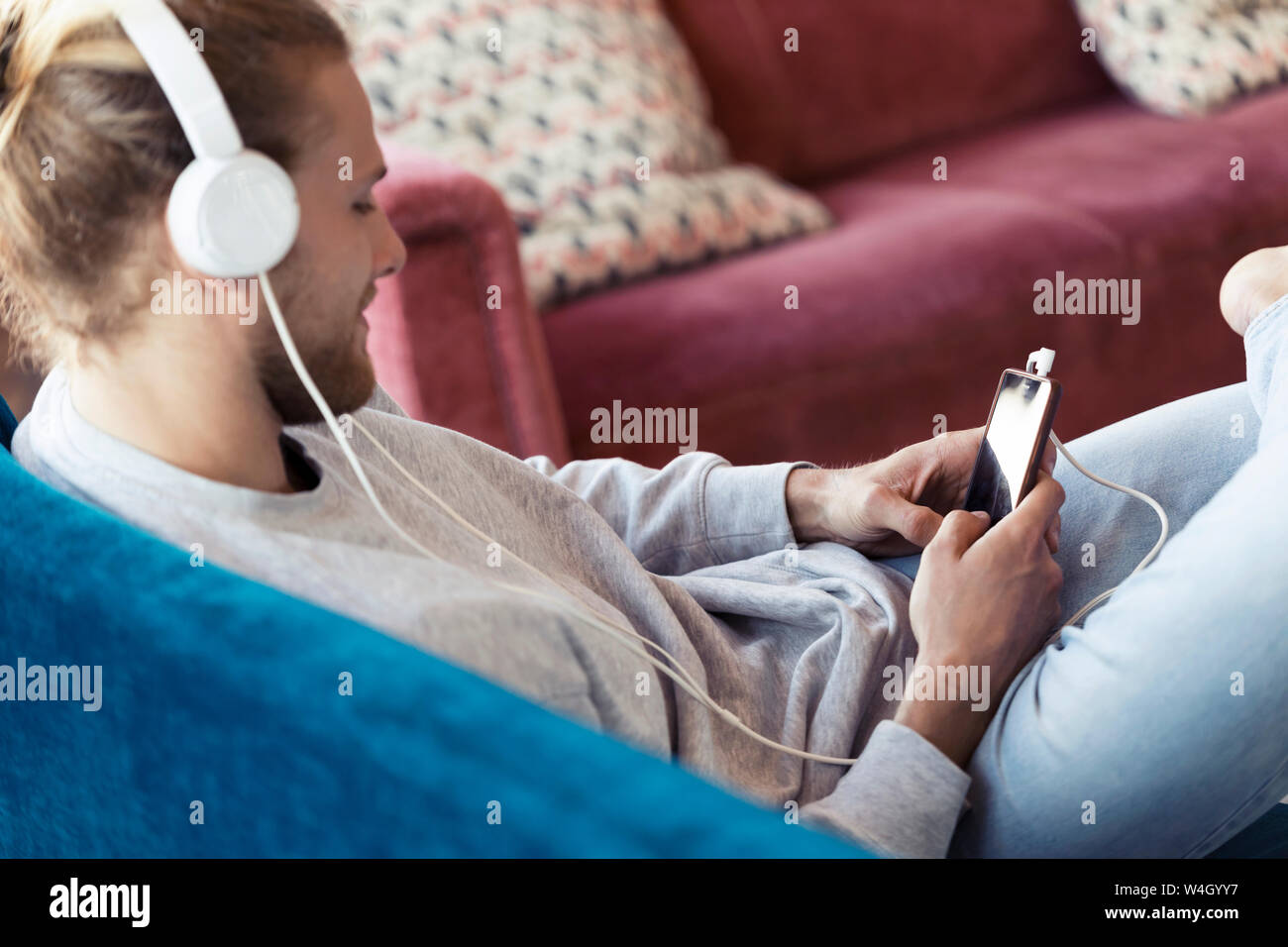 Young man sitting on couch with cell phone et écouteurs Banque D'Images