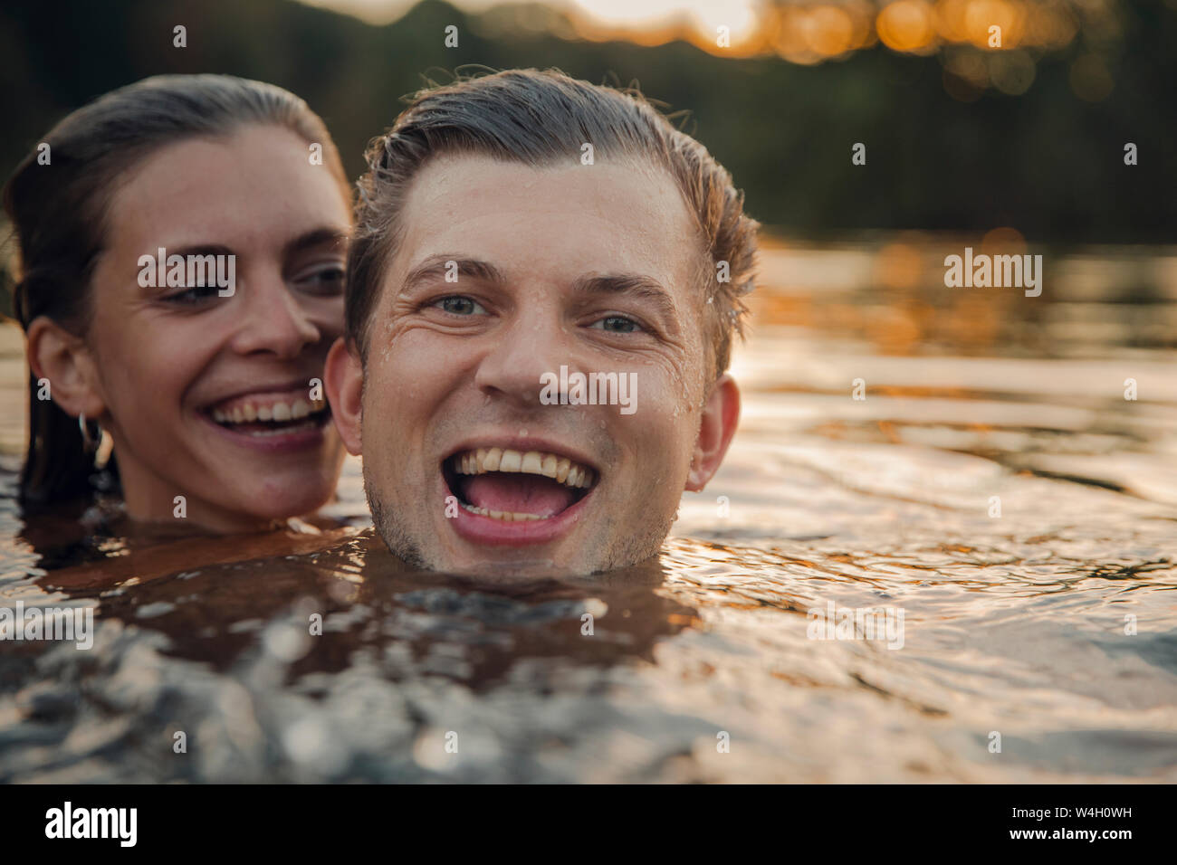 Jeune couple nager dans le lac au coucher du soleil Banque D'Images