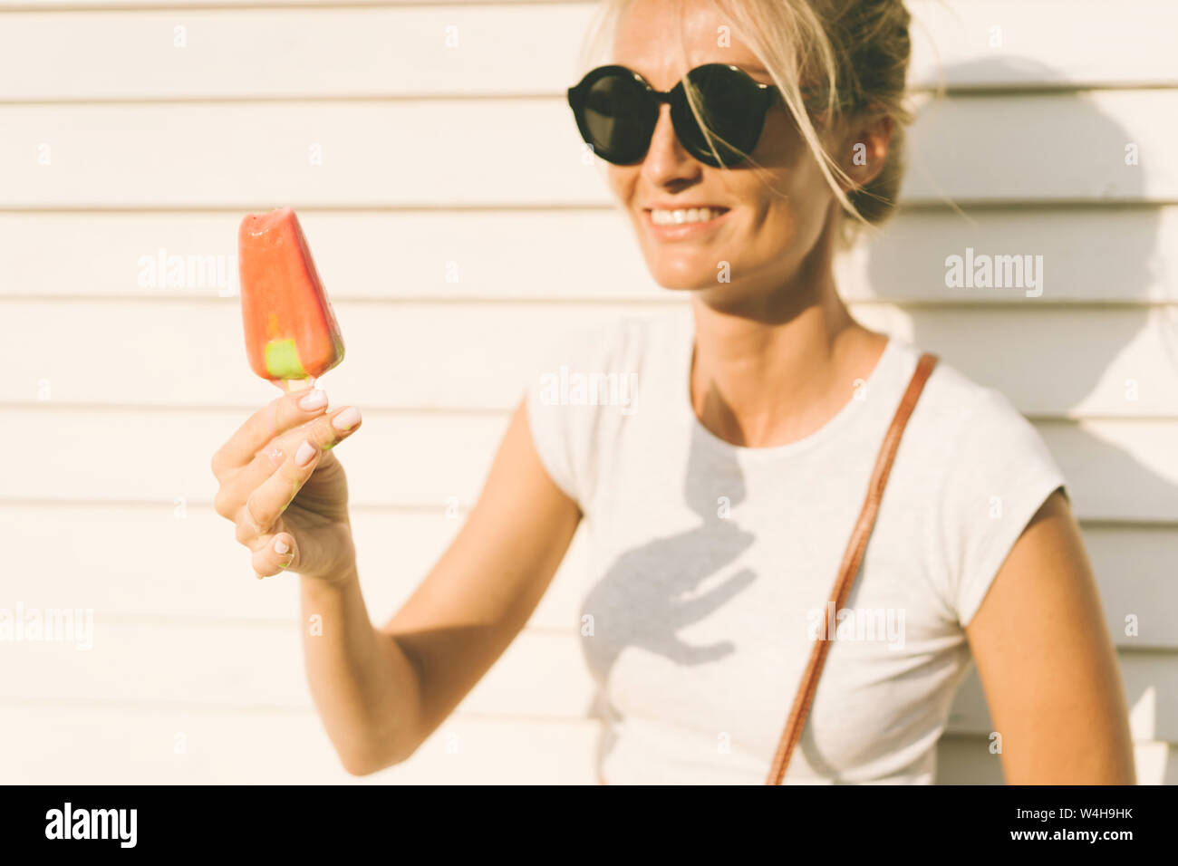 Une femme bronzée blanc à lunettes est titulaire d'un popsicle de fusion et de rires. Concept de vie d'été Banque D'Images