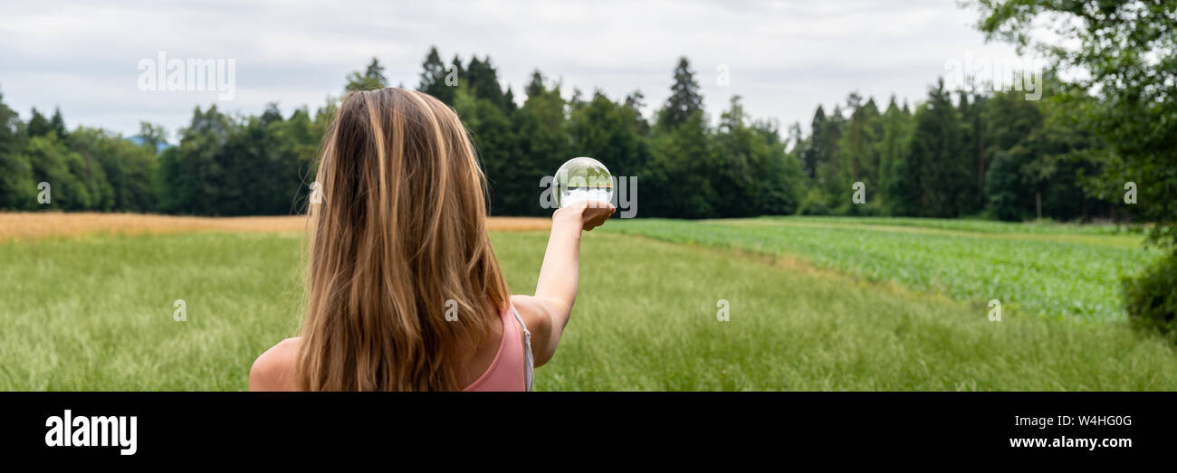 Vue de derrière d'une femme debout dans la nature entouré de champs et de prairies holding crystal ball dans sa main. Banque D'Images