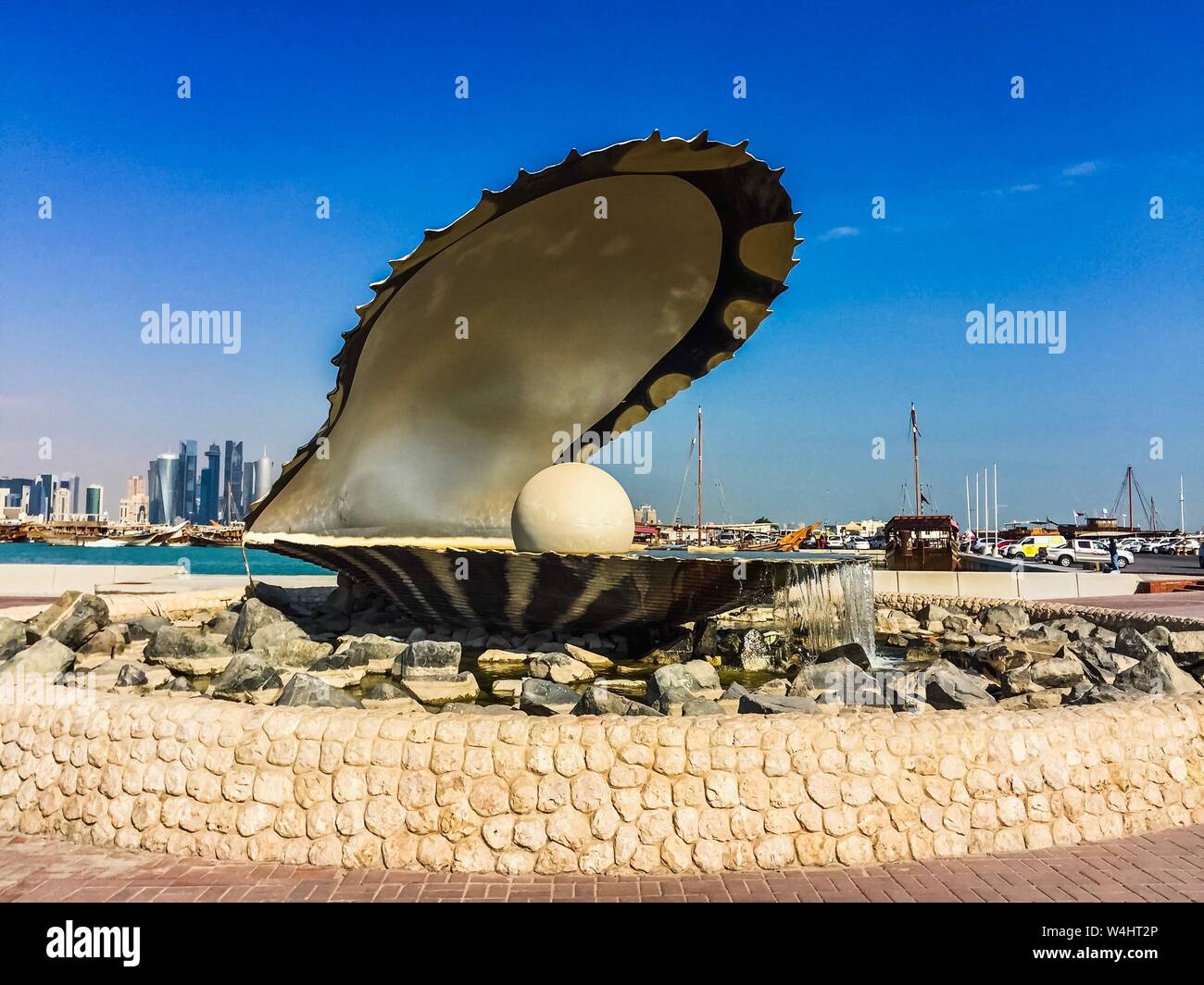 Le monument de la perle, une fontaine avec une sculpture d'huître et de perle, à la Corniche de Doha, Qatar, avec des bateaux et des bâtiments en arrière-plan. Banque D'Images