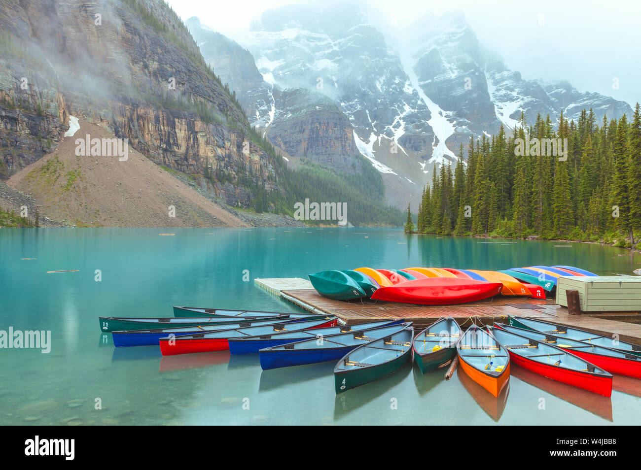 Des canoës colorés au lac Moraine, parc national Banff, Alberta, Canada, lors d'une journée d'été pluvieuse. Banque D'Images