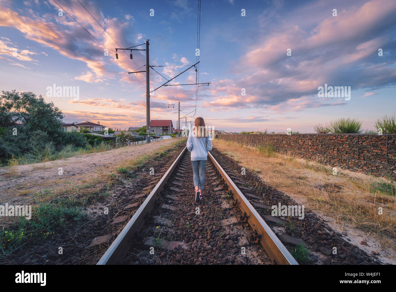 Jeune femme debout sur le chemin de fer au coucher du soleil en été Banque D'Images