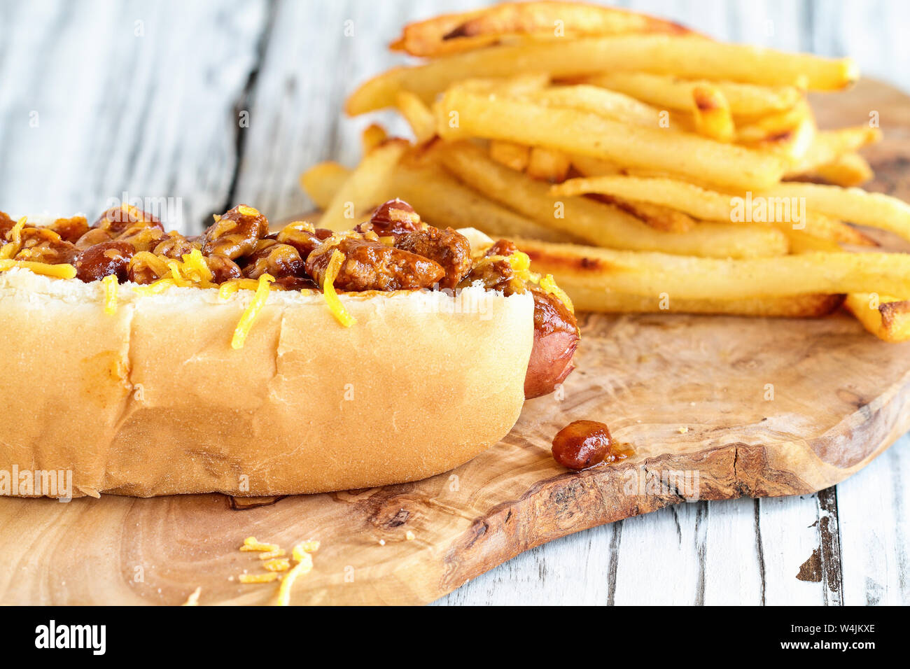 Hot dog avec du chili, fromage cheddar et la moutarde. Focus sélectif avec frites flou en arrière-plan. Banque D'Images