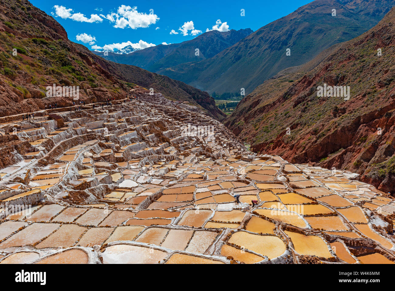 Terrasses de sel de Maras près de Cusco avec méconnaissable touristes entre les étangs de sel marche et les sommets enneigés des Andes, crête de montagne Salkantay au Pérou. Banque D'Images