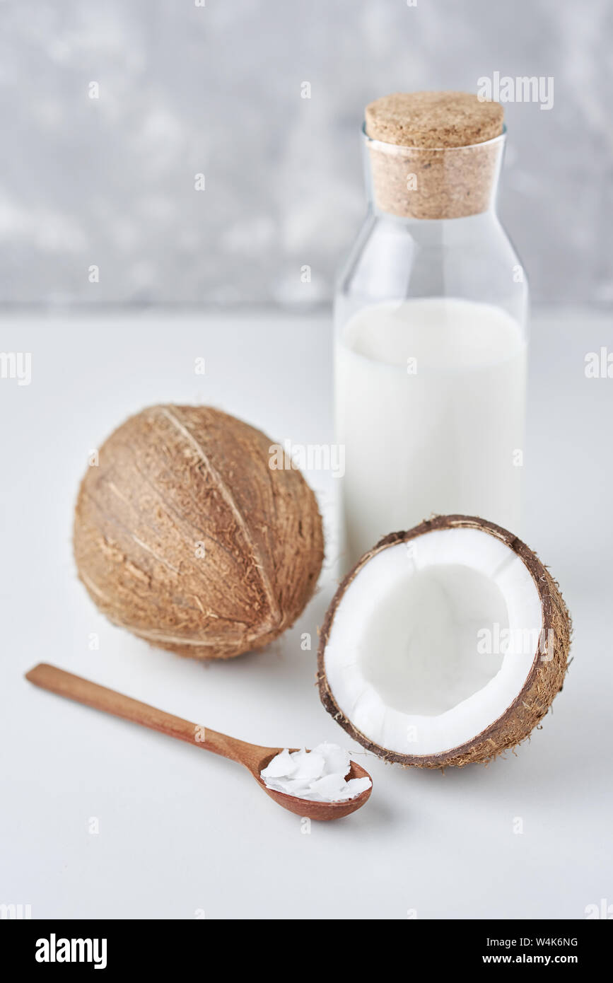 Le lait de coco en bouteille en verre et de coco fraîche avec la moitié sur fond gris Banque D'Images