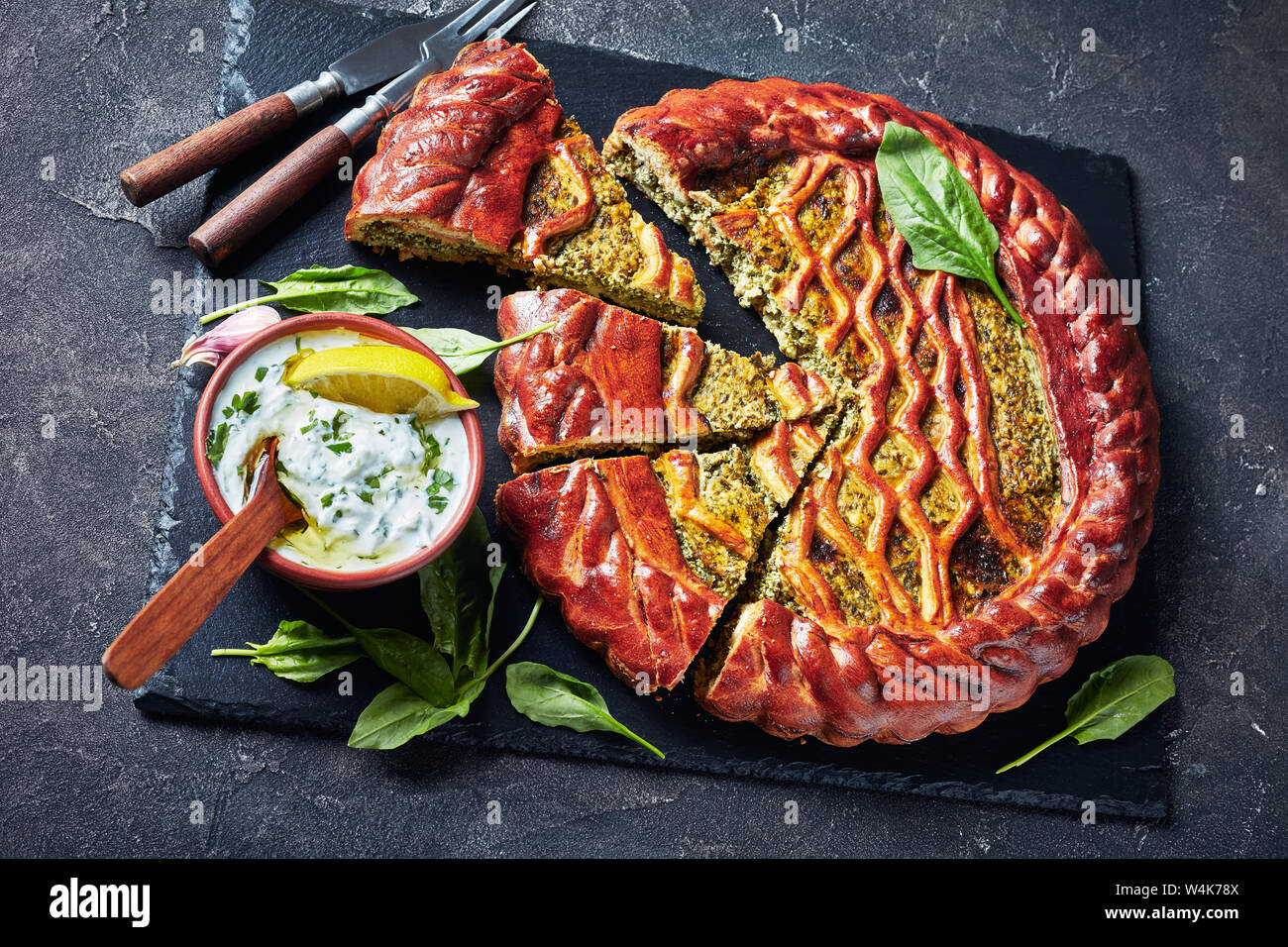 Les Épinards quiche Ricotta en tranches sur un plateau en ardoise noire avec sauce tzatziki dans un bol sur une table, vue de dessus Banque D'Images