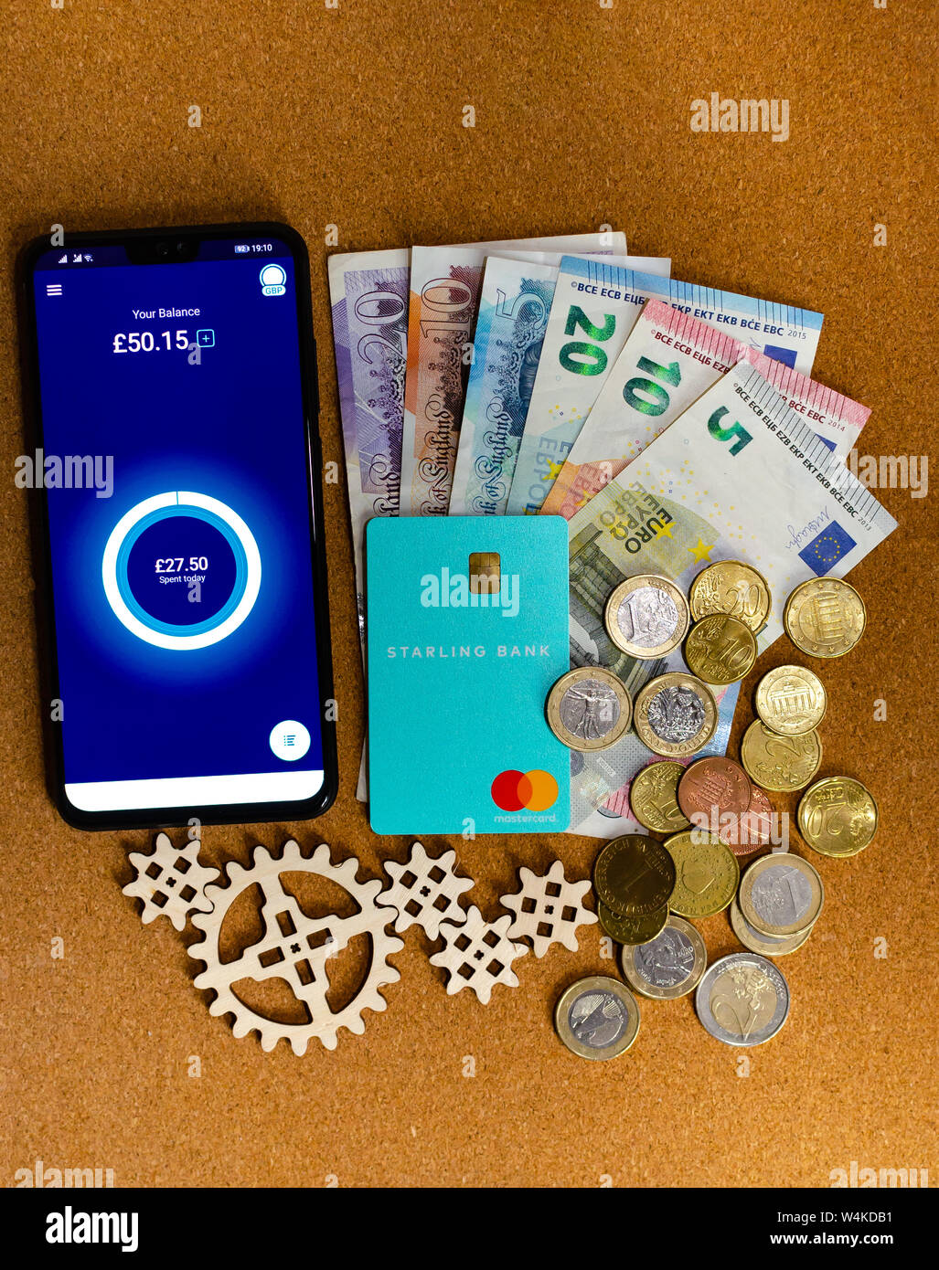 Carte de banque, l'Étourneau sansonnet app sur l'écran du smartphone et certains billets, de pièces et d'engrenages en bois autour. Image conceptuelle pour Banque Starling Banque D'Images