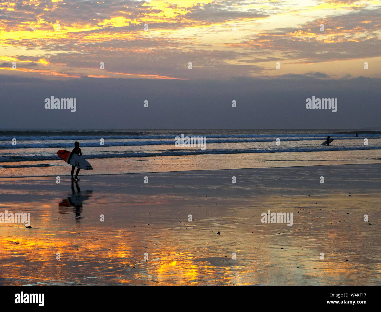 Boy with surfboard promenades le long de la plage de Kuta au coucher du soleil Banque D'Images