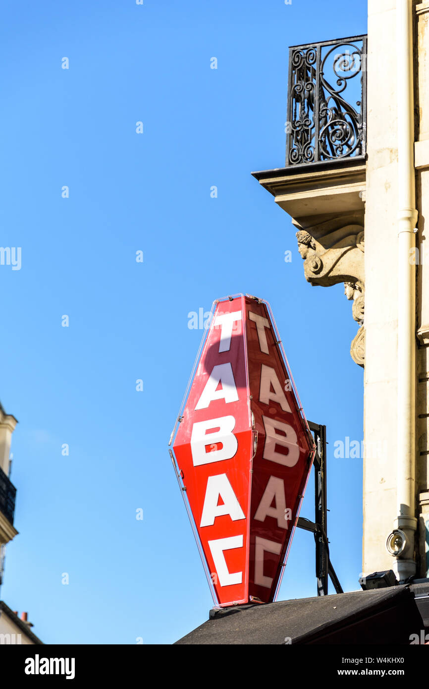Magasin de tabac français rouge signe avec lettrage blanc et immeuble haussmannien en arrière-plan sur fond de ciel bleu. Banque D'Images