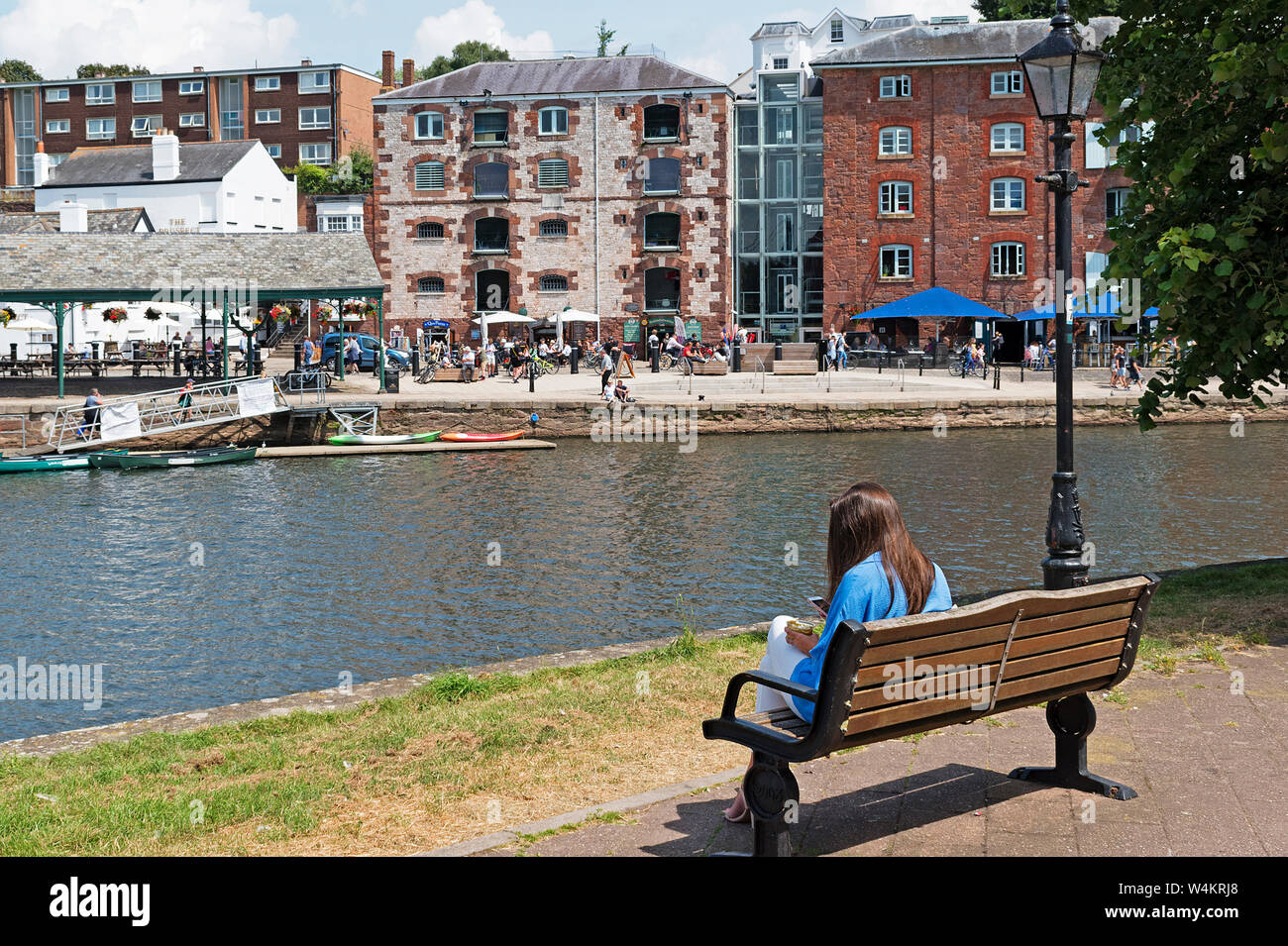 Jeune femme assise sur un banc près de la rivière exe à Exeter, Devon, Angleterre, Grande-Bretagne, Royaume-Uni. Banque D'Images